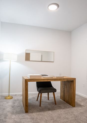 Desk with a chair and a lamp in a room with white walls and carpet